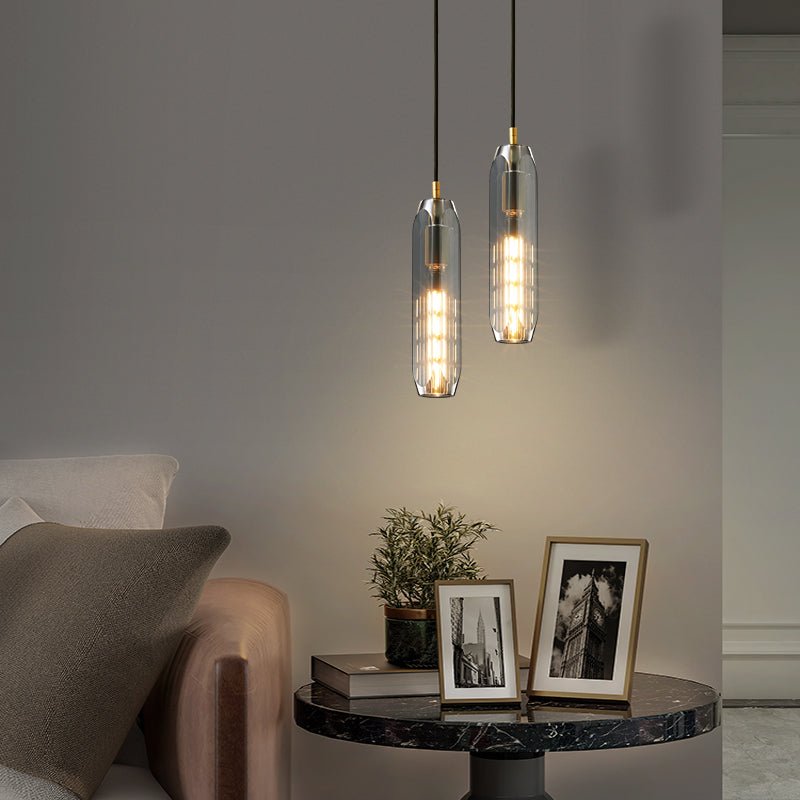 Two smoke grey glass Clérachic pendants hang at different heights above a round marble table with framed photographs.