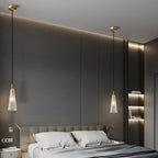 Two textured clear glass Clérachic pendants hang on either side of a bed, with a cove-lit grey panelled wall behind.