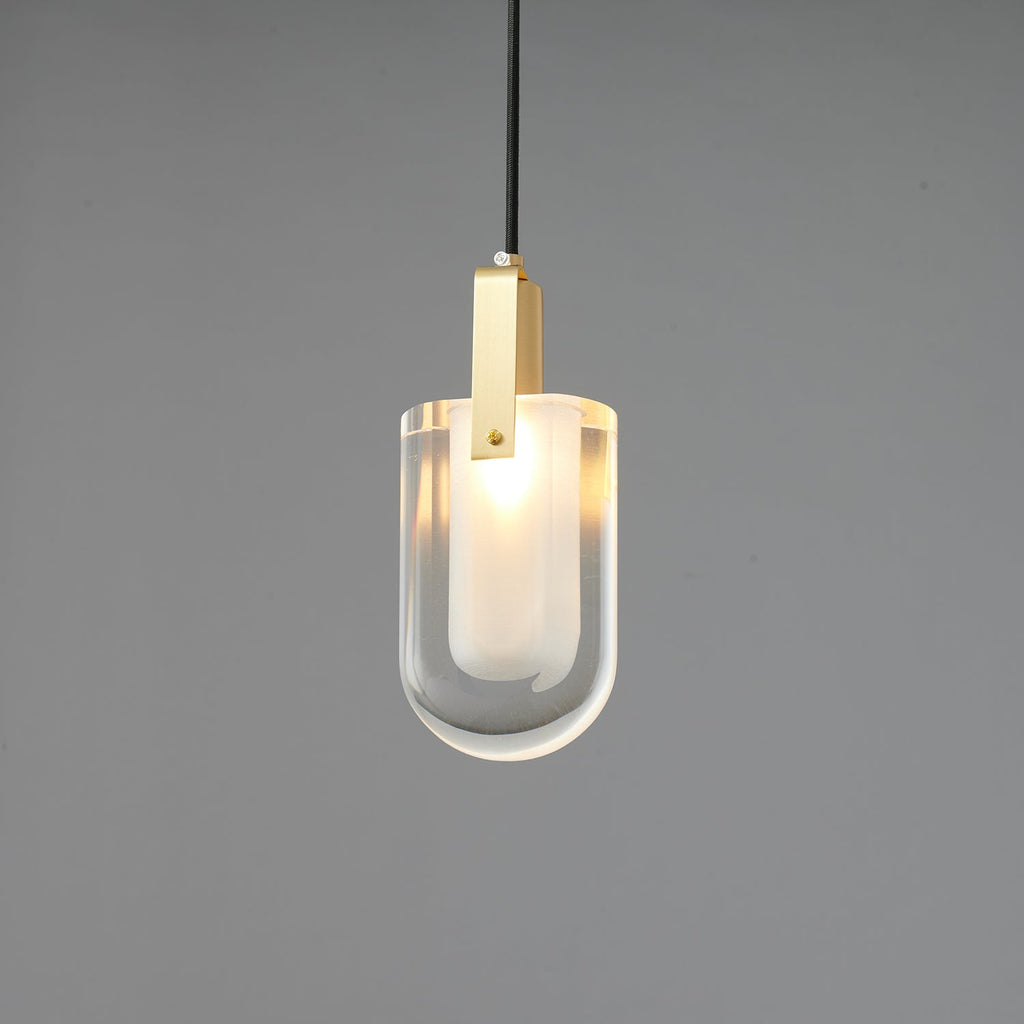 A smaller view of the lit U-shaped Clérachic pendant, with a brass bracket and a clear glass outer shade on grey.