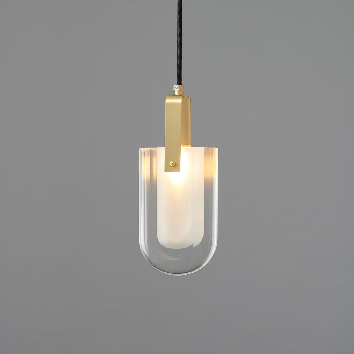 Slightly wider U-shaped Clérachic pendant, with its glass edge catching the light above a frosted liner, on a grey backdrop.