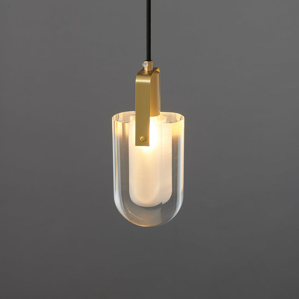 A close view of the lit U-shaped Clérachic pendant, showing the brushed brass bracket and the glow of the frosted liner.