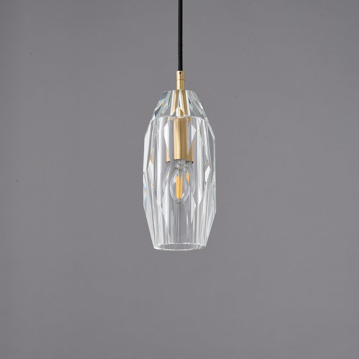 A Clérachic pendant with a faceted clear glass shade around a brass lamp holder, unlit on a grey backdrop.