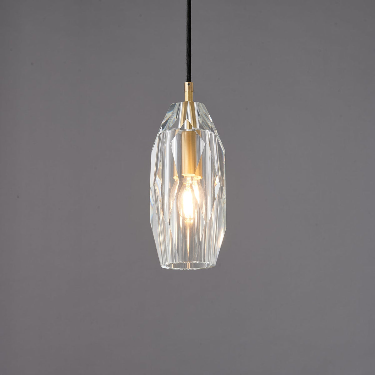 The faceted clear glass Clérachic pendant lit, with the filament bulb glowing through the cut glass.