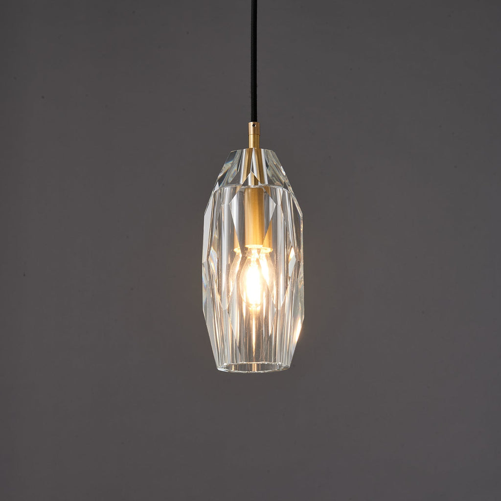 The faceted glass Clérachic pendant lit warm against a darker grey backdrop, with light playing across the cut facets.