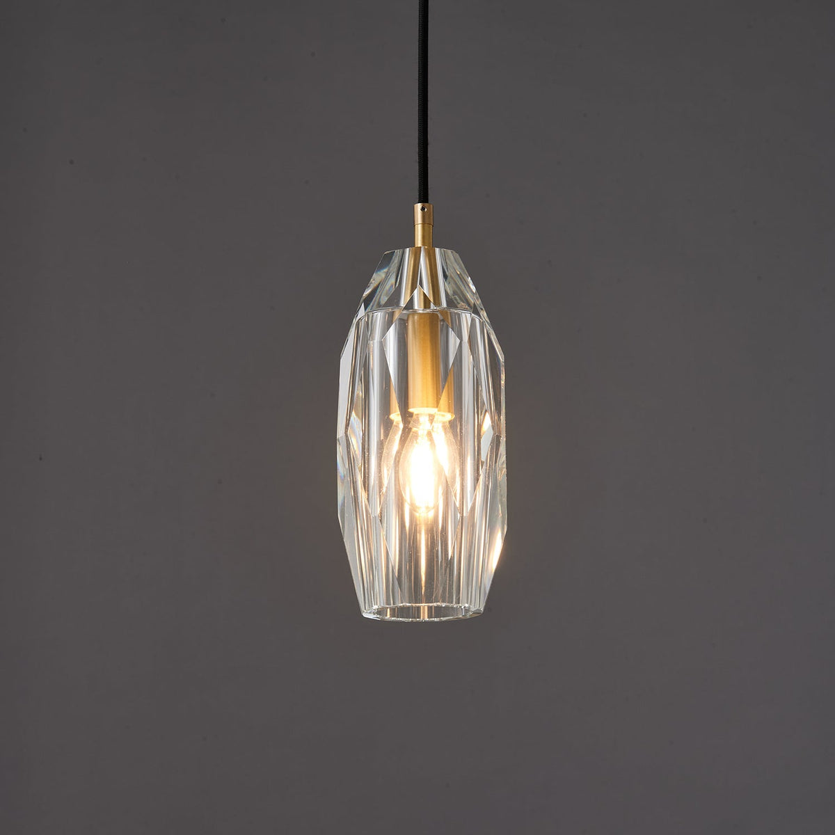 The faceted glass Clérachic pendant lit warm against a darker grey backdrop, with light playing across the cut facets.
