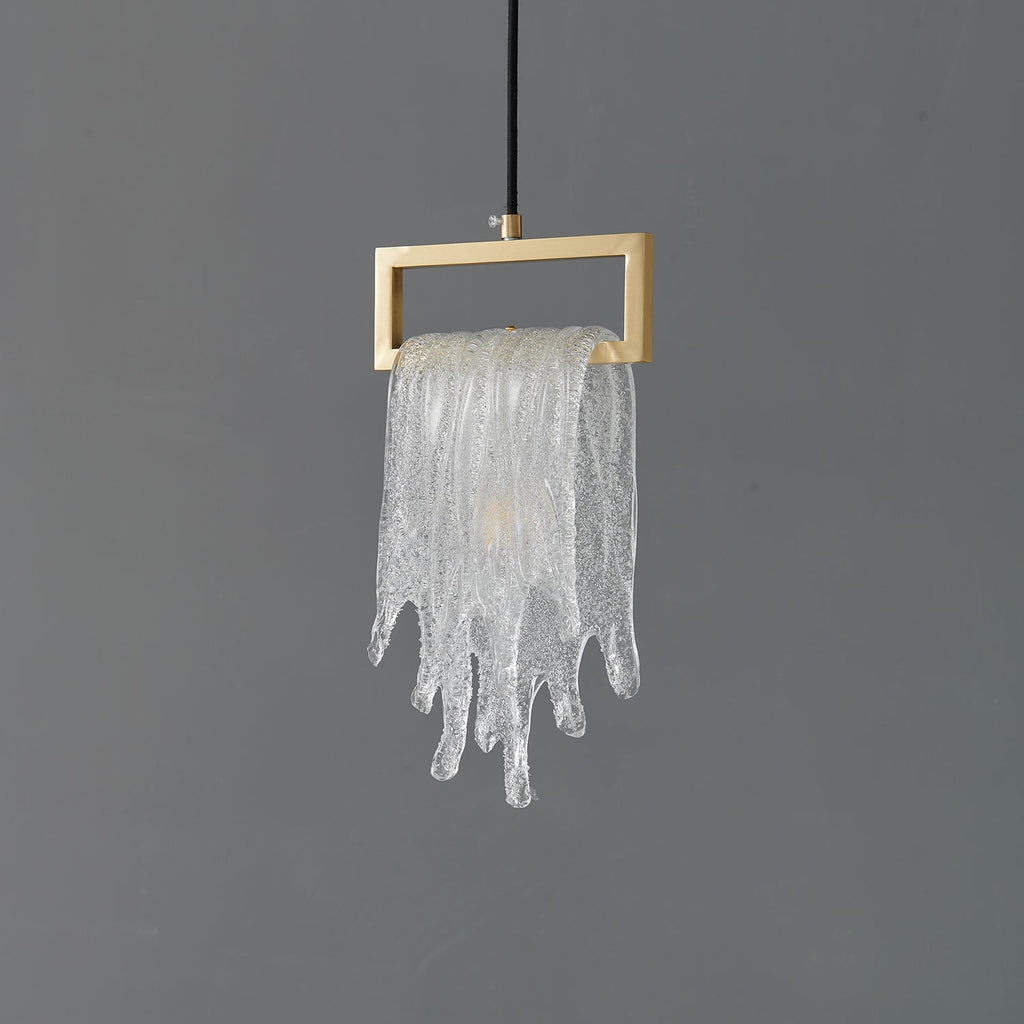 A Clérachic pendant with a frosted, icicle-like glass drape over a brass rectangular frame, unlit on grey.
