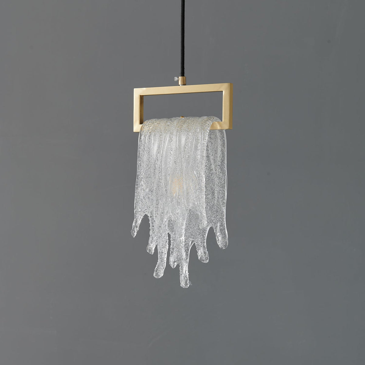 A Clérachic pendant with a frosted, icicle-like glass drape over a brass rectangular frame, unlit on grey.