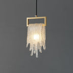 The same draped glass Clérachic pendant, lit, with the icicle-like glass glowing warm below a brass frame.