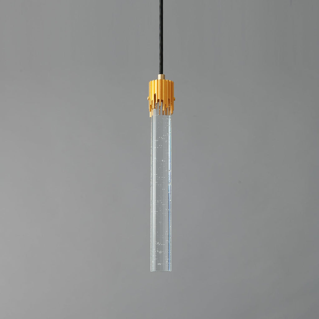 A Clérachic pendant with a long clear glass rod flecked with tiny bubbles and a ribbed brass cap, unlit on grey.