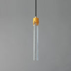 A Clérachic pendant with a long clear glass rod flecked with tiny bubbles and a ribbed brass cap, unlit on grey.