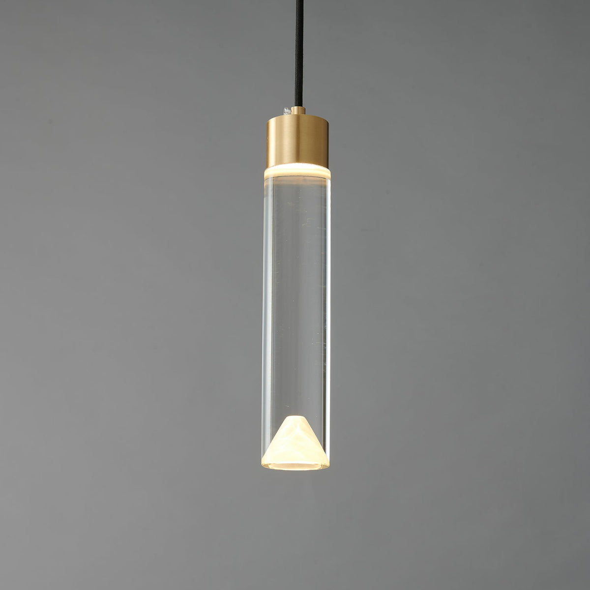 The glass cylinder Clérachic pendant lit, with a bright ring at the brass cap and a glowing cone at the base.