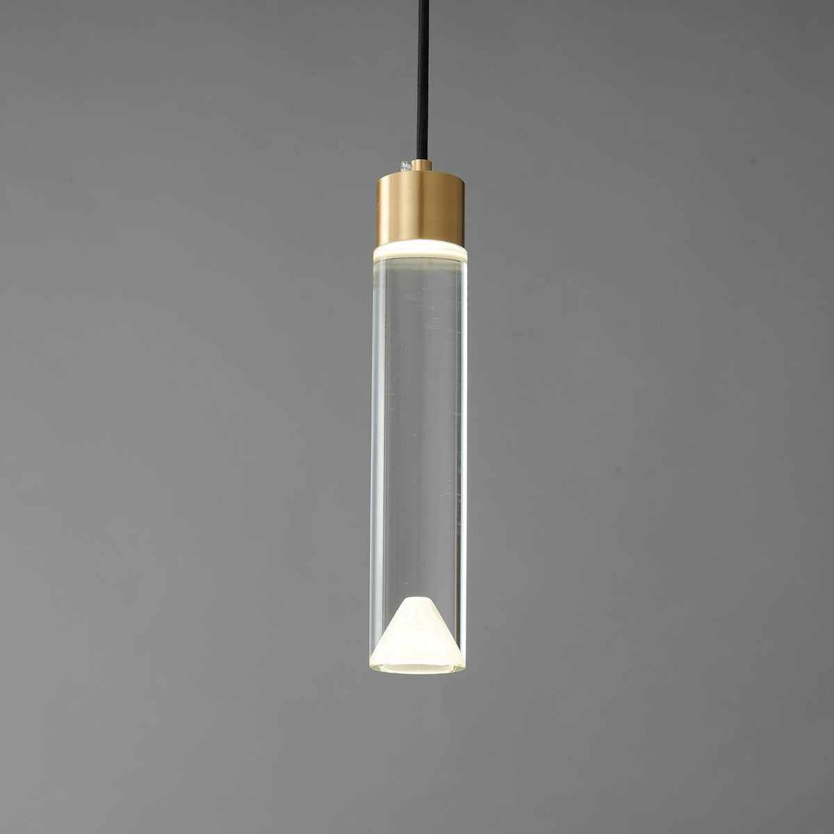 The lit cylinder Clérachic pendant on a dark grey backdrop, with the glow concentrated at both ends of the clear glass.