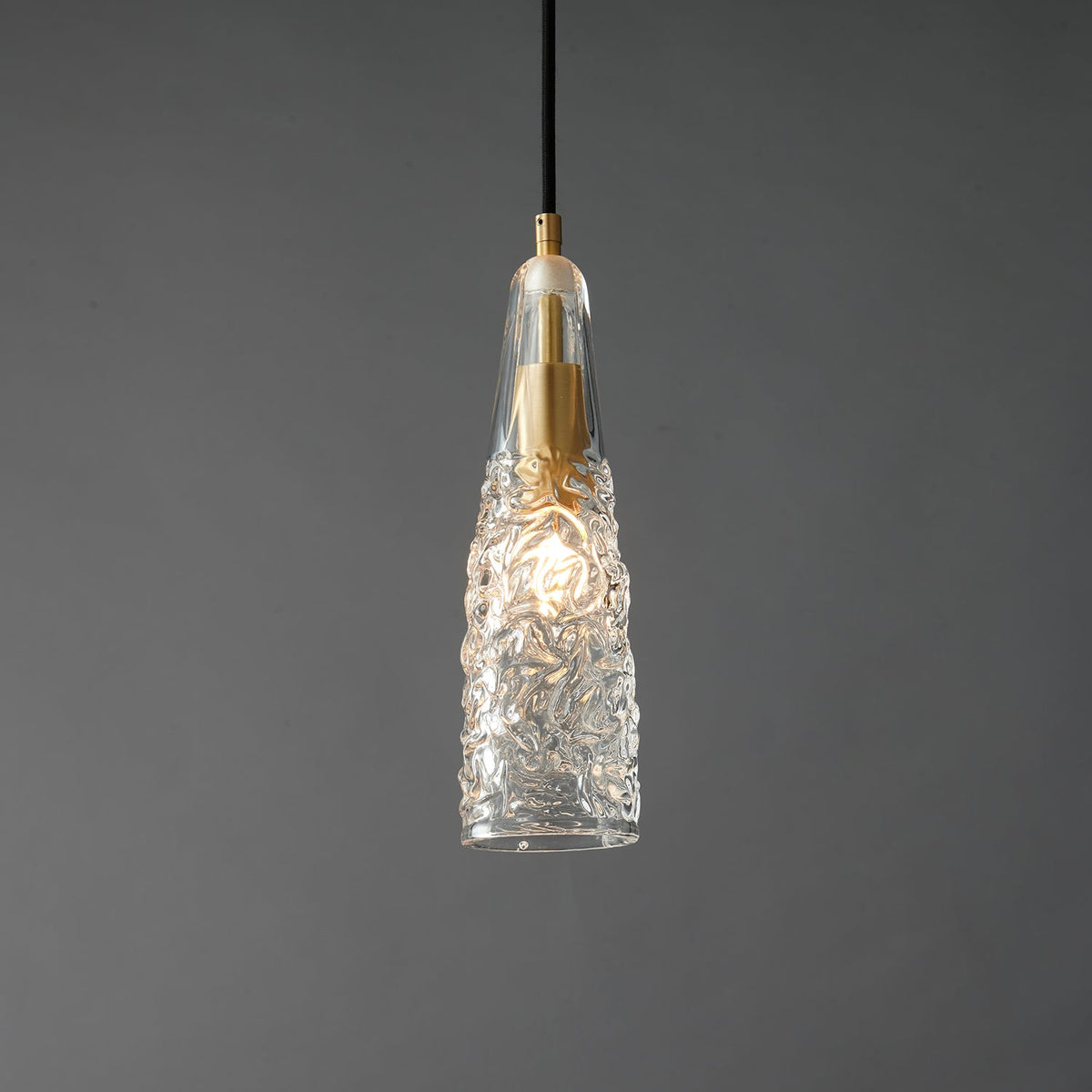 Close view of the lit crinkled glass Clérachic pendant, with the bulb glowing through the textured clear shade.