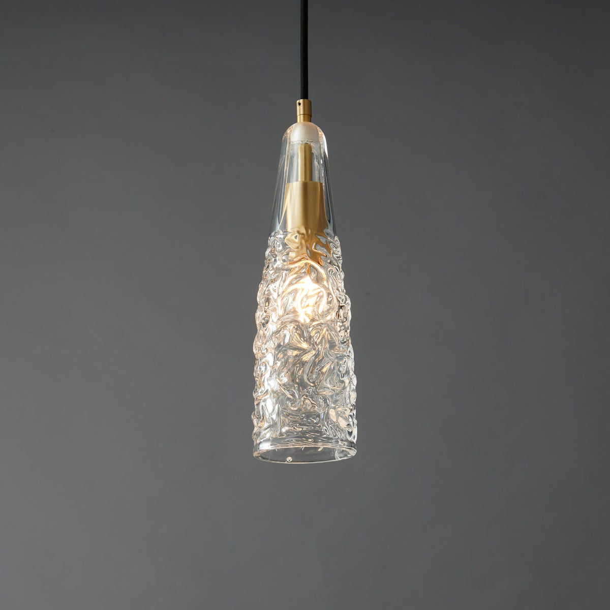 A lit Clérachic pendant with a crinkled glass shade, with a bright bulb glow inside and a brass fitting at the top.
