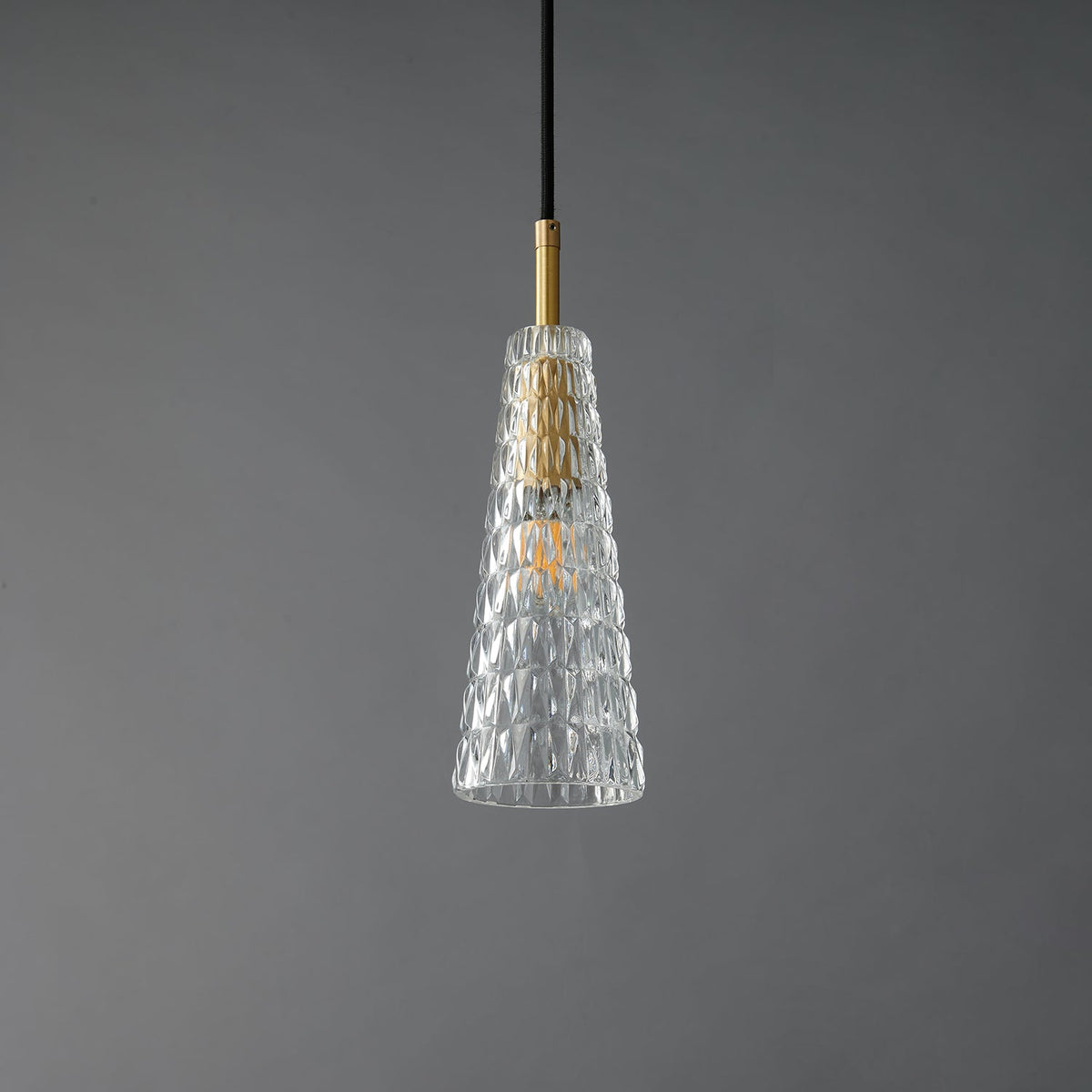 A Clérachic pendant with a tapered clear shade moulded in a diamond pattern, around a brass fitting and a filament bulb, unlit.