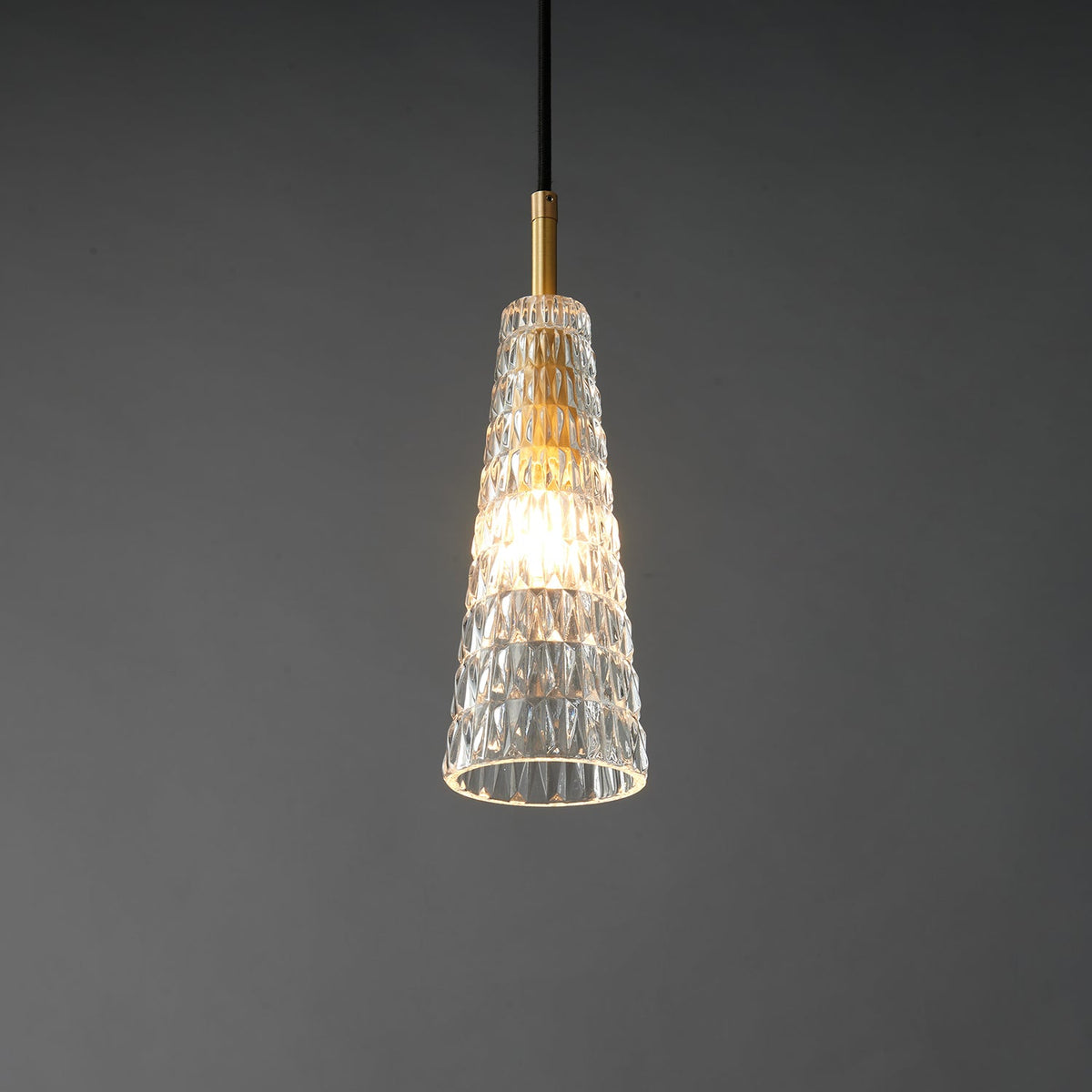 A brighter view of the lit diamond-patterned Clérachic pendant, with a warm centre glow and a brass fitting above.