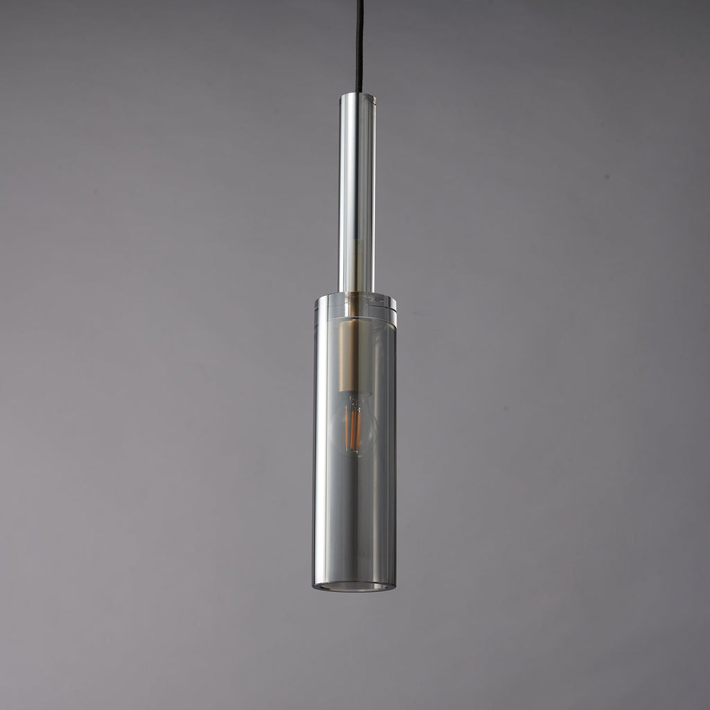 A Clérachic pendant with a slim smoke grey glass cylinder and a clear glass tube above it, unlit against a grey wall.