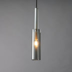 The smoke grey cylinder Clérachic pendant lit, with a warm filament bulb glowing inside the tinted glass.
