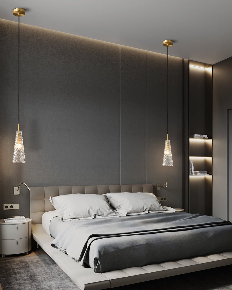 Two Clérachic pendants with textured clear glass shades hang either side of a bed in a dark bedroom with cove lighting.