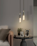Two smoke grey Clérachic pendants hang beside a sofa and a round marble table with framed photos, in a portrait view.