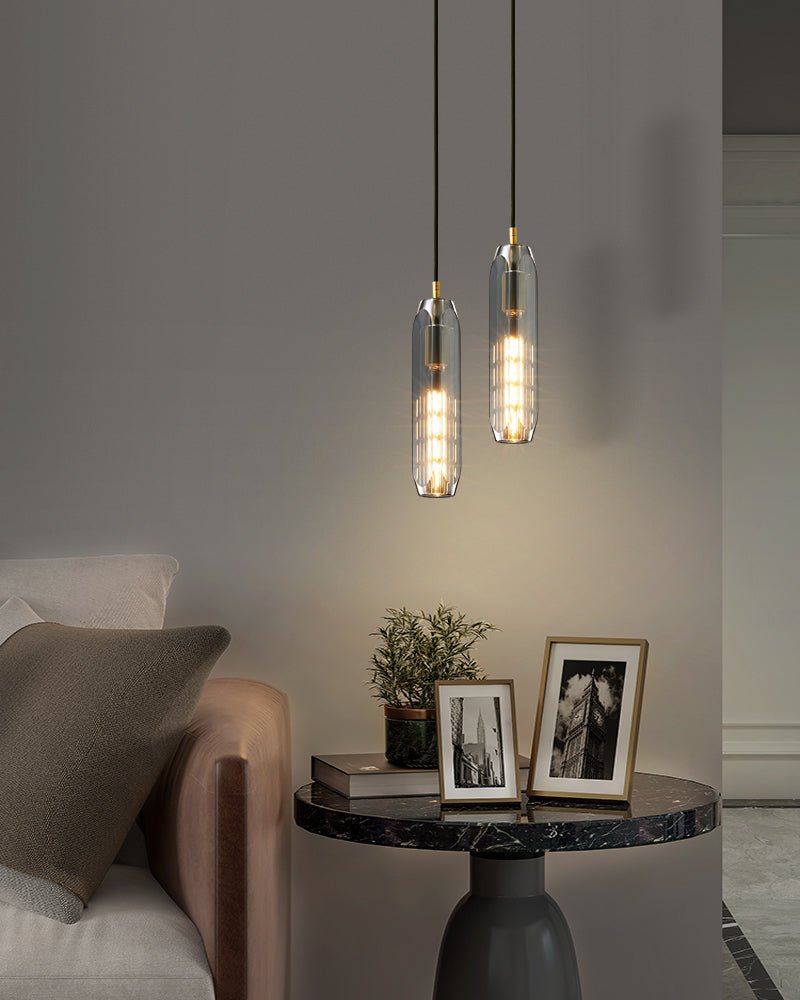 Two smoke grey Clérachic pendants hang beside a sofa and a round marble table with framed photos, in a portrait view.