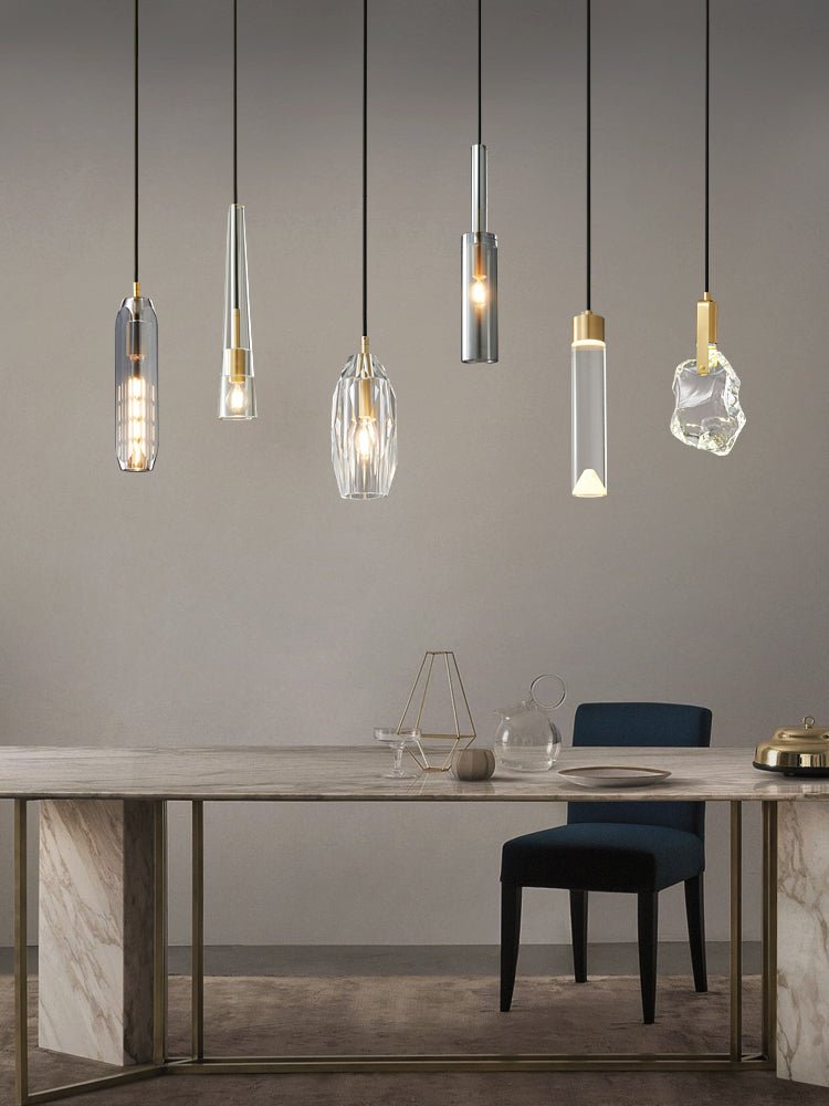 Six Clérachic pendants in varied glass shapes hang over a marble table with a navy chair, in a taller frame.