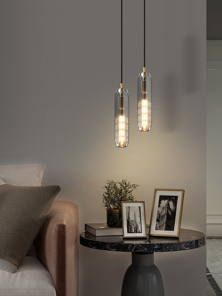 Two smoke grey glass Clérachic pendants hang above a marble table, framed photographs and a plant, in a taller view.