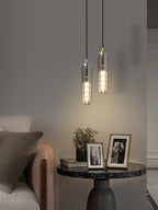 Two smoke grey glass Clérachic pendants hang above a marble table, framed photographs and a plant, in a taller view.