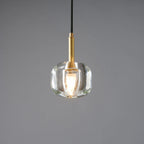A Clérachic pendant with a rounded, thick clear glass shade and a brass stem, with a lit bulb inside, on a grey backdrop.