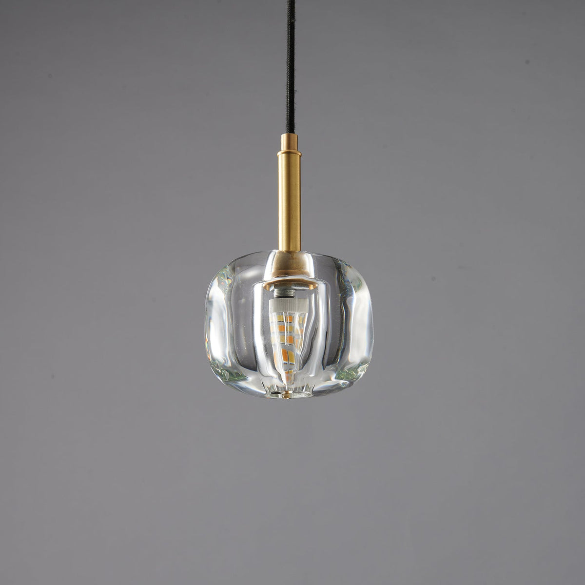The rounded clear glass Clérachic pendant with a warm filament bulb inside, shown against a grey backdrop.