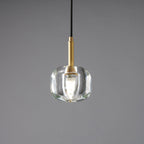 A smaller Clérachic pendant with a rounded, thick clear glass shade and a brass stem, lit on a grey backdrop.