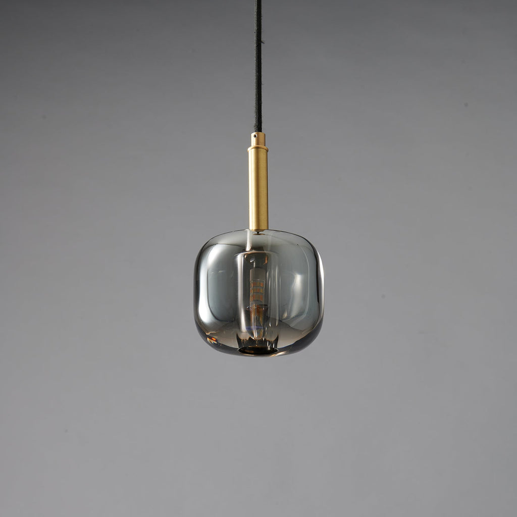 A Clérachic pendant with a rounded smoke grey glass shade and a brass stem, unlit on a grey backdrop.