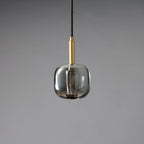 A Clérachic pendant with a rounded smoke grey glass shade and a brass stem, unlit on a grey backdrop.