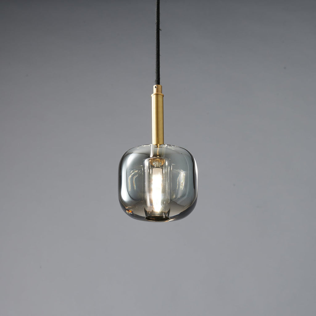 The rounded smoke grey Clérachic pendant lit, with a bright bulb glowing inside the tinted glass.