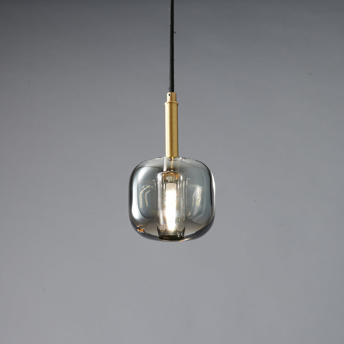 The rounded smoke grey Clérachic pendant lit, with a bright bulb glowing inside the tinted glass.