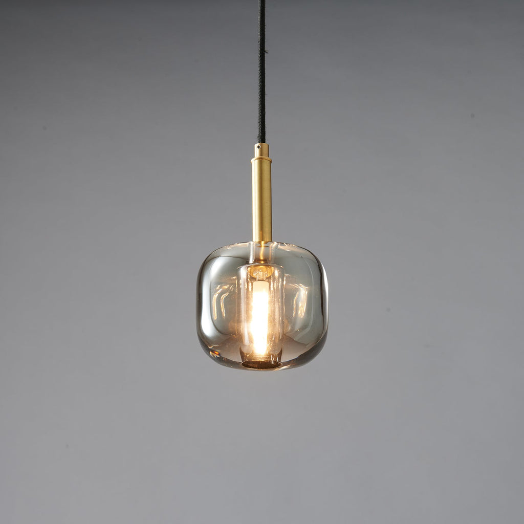 A rounded smoke grey Clérachic pendant lit warm, with a brass stem and black cord on a grey backdrop.
