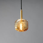 A Clérachic pendant with a rounded amber glass shade and a brass stem, lit warm on a grey backdrop.