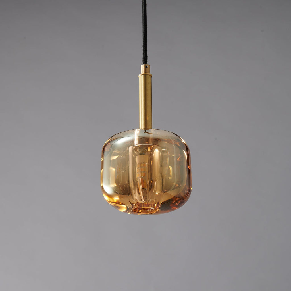 A Clérachic pendant with a rounded, honey-toned amber glass shade, lit, with a brass stem above it.