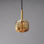 A Clérachic pendant with a rounded, honey-toned amber glass shade, lit, with a brass stem above it.