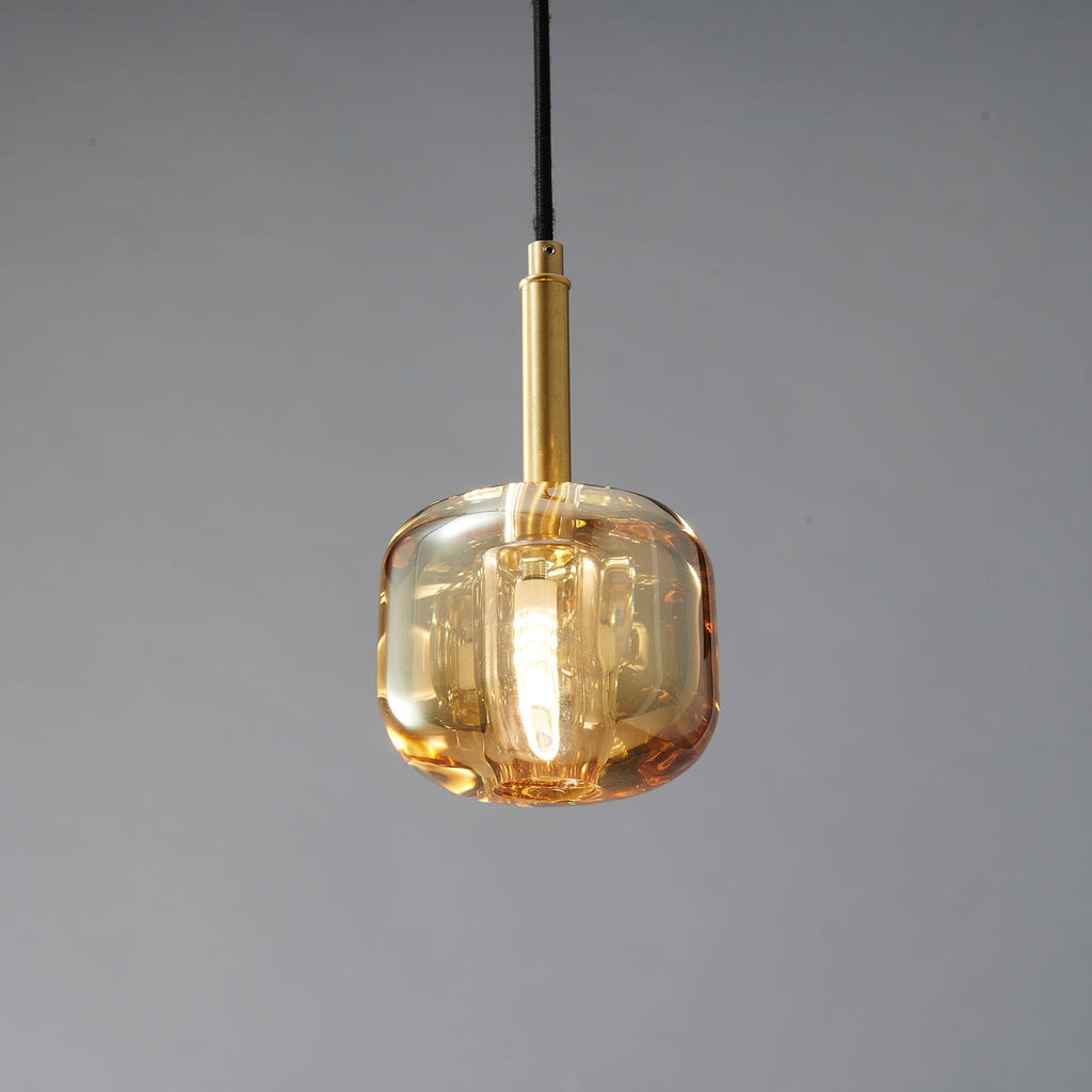 A closer view of the amber glass Clérachic pendant, with a brass stem and a warm glow in the thick glass.