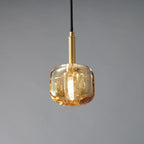 A closer view of the amber glass Clérachic pendant, with a brass stem and a warm glow in the thick glass.