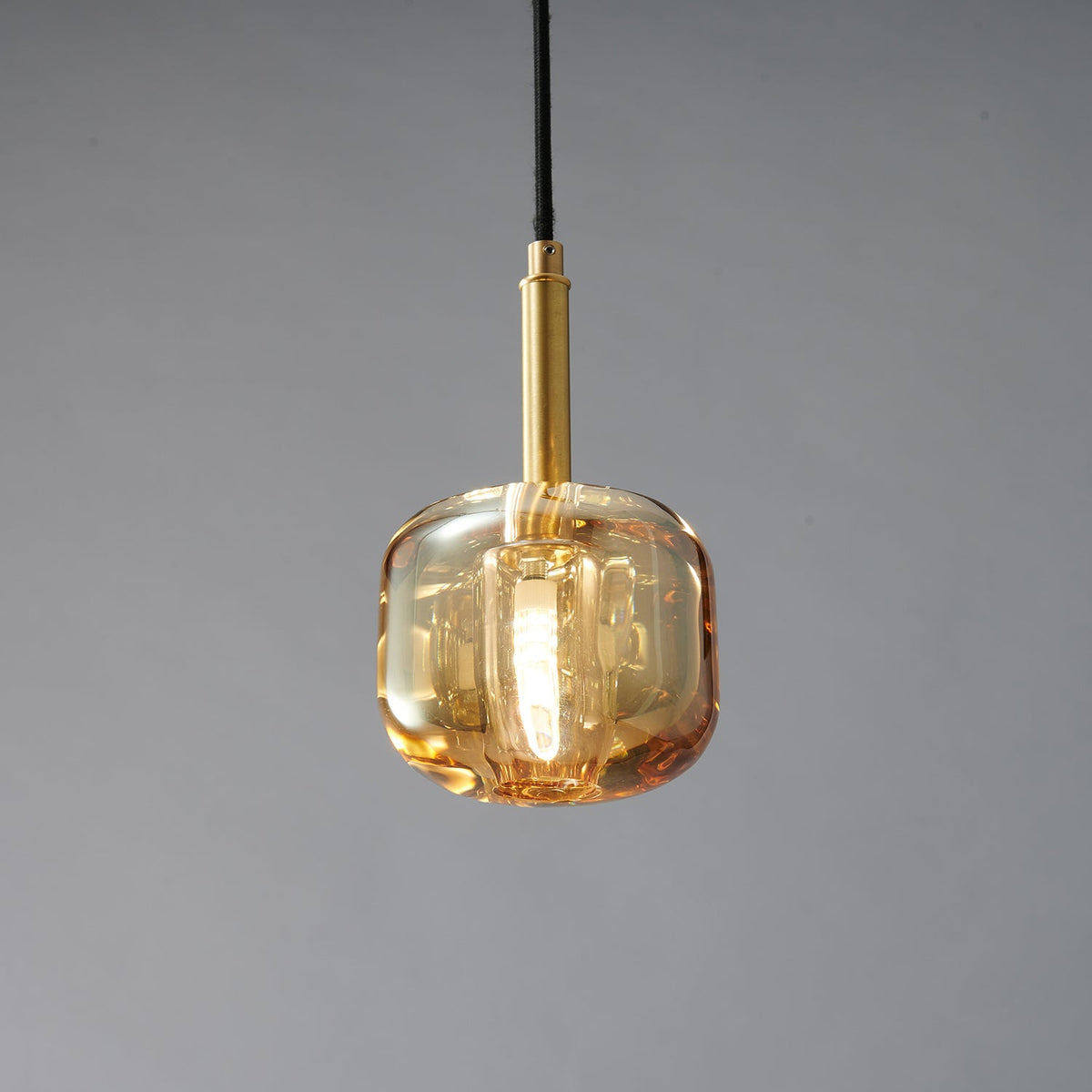 A closer view of the amber glass Clérachic pendant, with a brass stem and a warm glow in the thick glass.