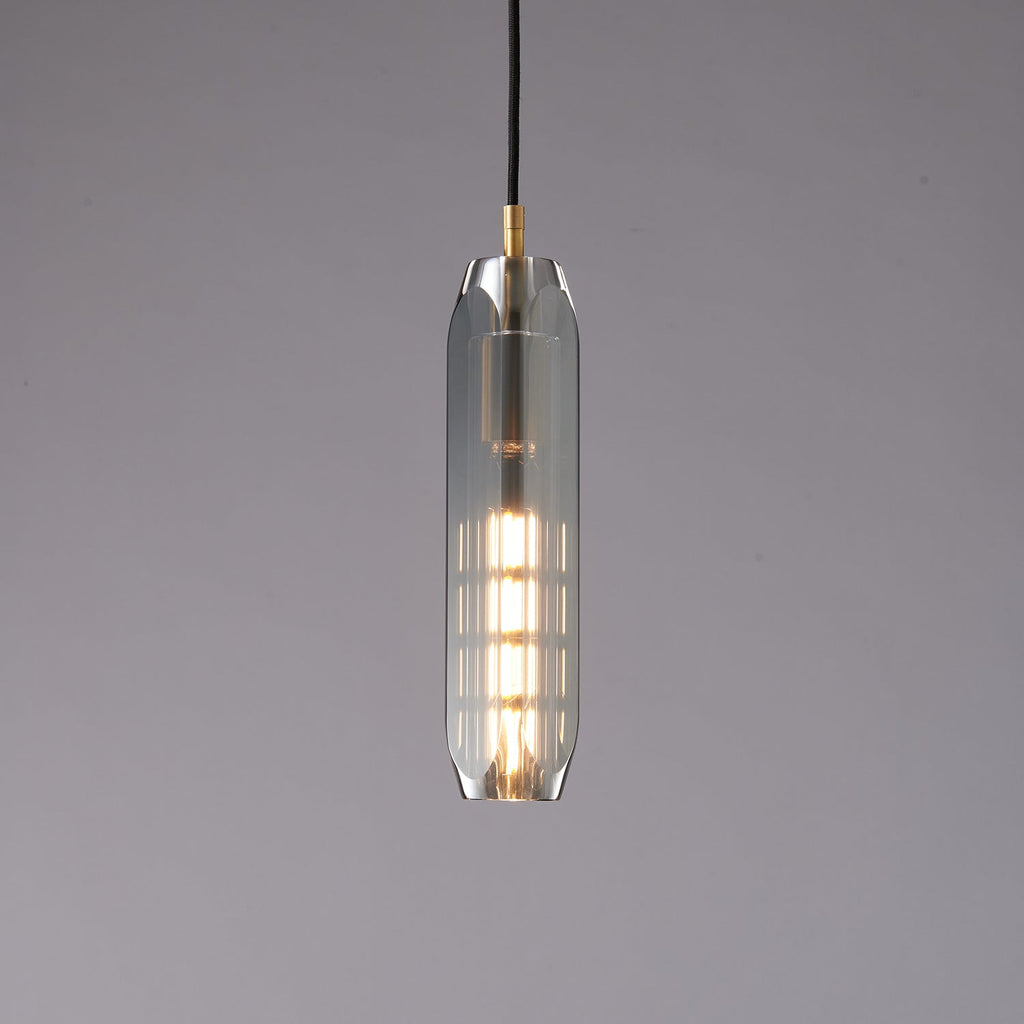 A tall, slim Clérachic pendant with a smoke grey glass shade, lit from within by a long filament bulb, on a grey backdrop.