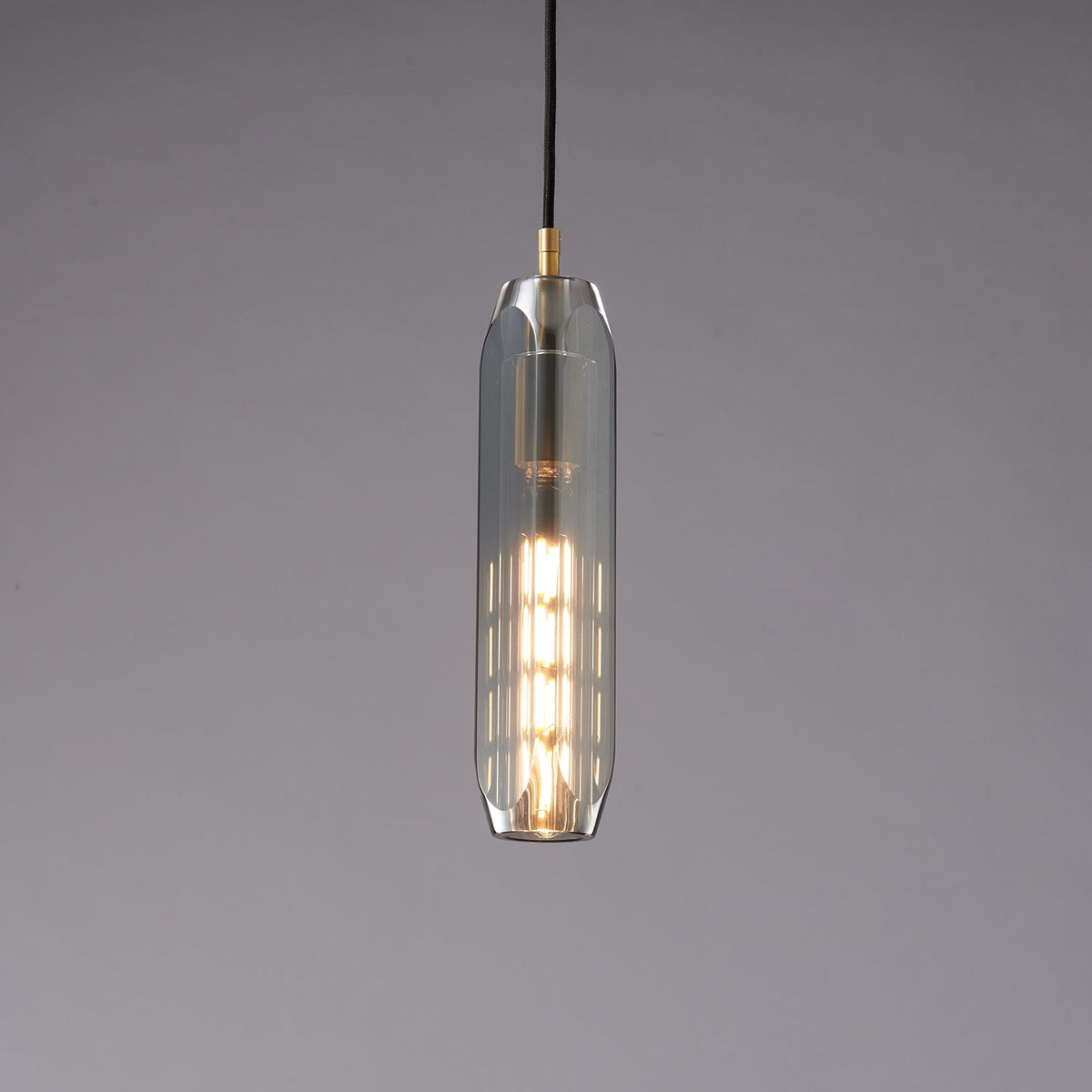 The slim smoke grey Clérachic pendant lit, with a stack of glowing filament segments visible through the glass.