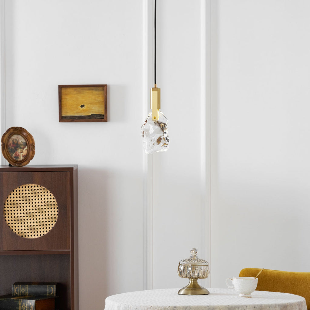 The rock-like glass Clérachic pendant hangs near a dark wooden cabinet with a cane panel and a small framed painting.