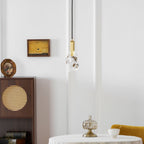 The rock-like glass Clérachic pendant hangs near a dark wooden cabinet with a cane panel and a small framed painting.