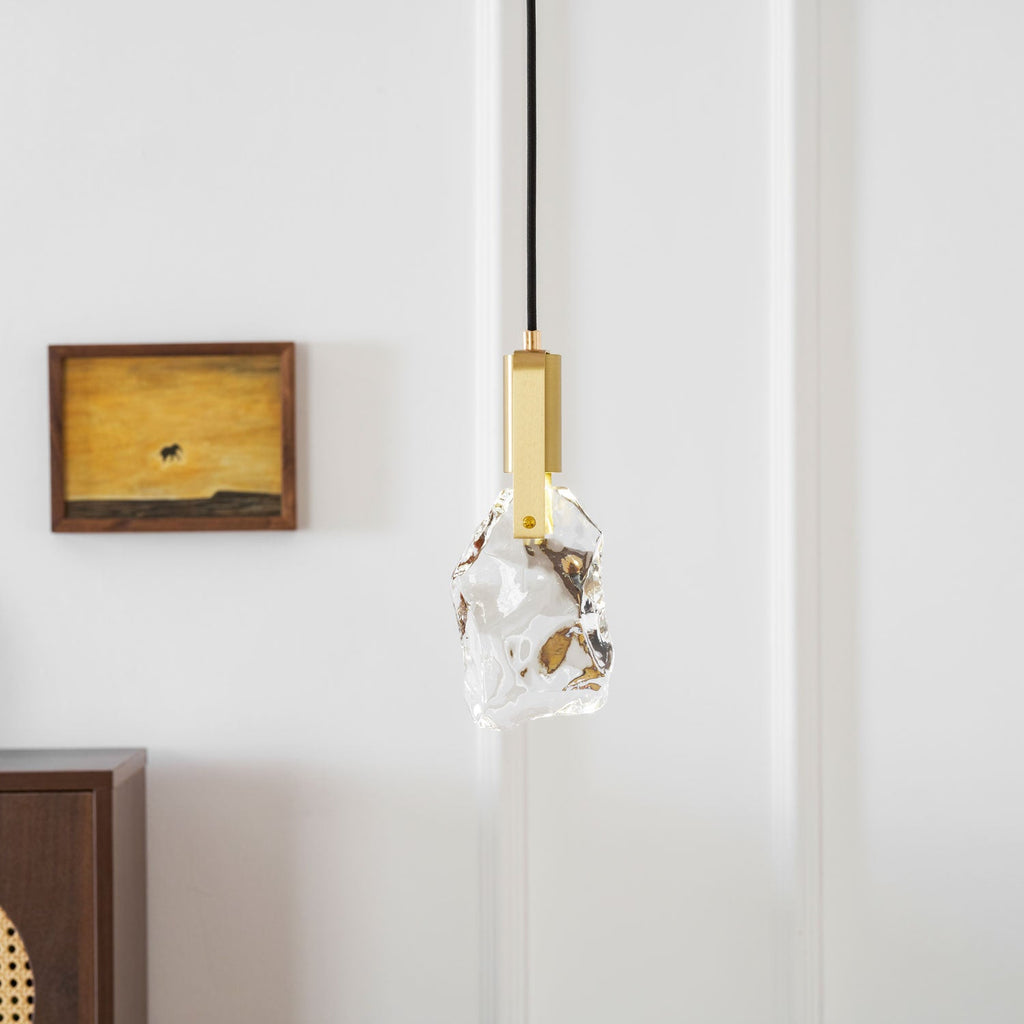 A closer view of the rock-like glass Clérachic pendant and its brass bracket, with a framed painting behind it.