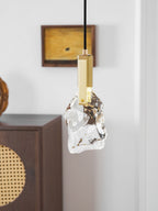 Rock-like clear glass on this Clérachic pendant, with a brass bracket, in front of a white panelled wall and a cabinet.