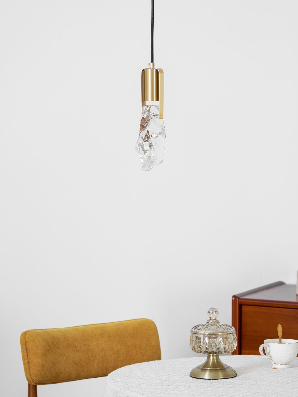 A small rock-glass Clérachic pendant with a round brass cap hangs above a table with a yellow chair and a cup.