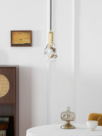 A slightly smaller view of the rock-glass Clérachic pendant by a white wall, a framed painting and a wooden cabinet.